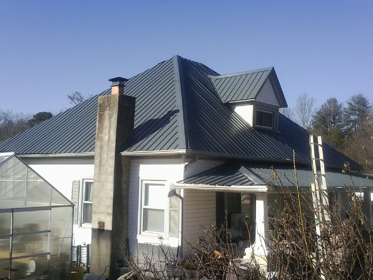 Dark blue standing seam metal roof on a white farmhouse with dormer — Slate & Tile Roof Repair by Roofing Brothers in Clarendon