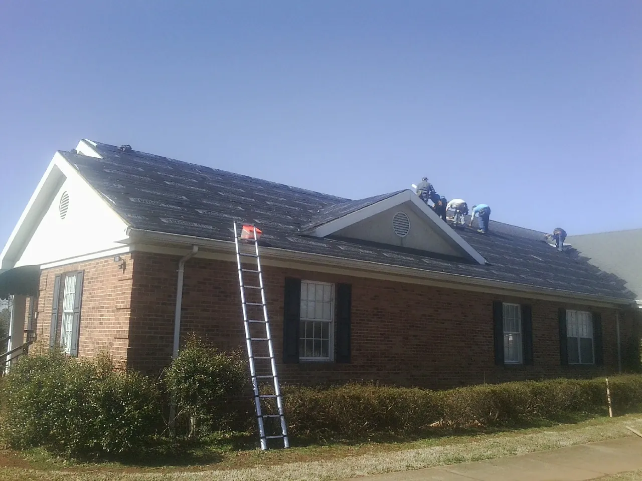 Crew tearing shingles off a brick ranch roof with a ladder set — Emergency Roof Repair work by our crew in Clarendon
