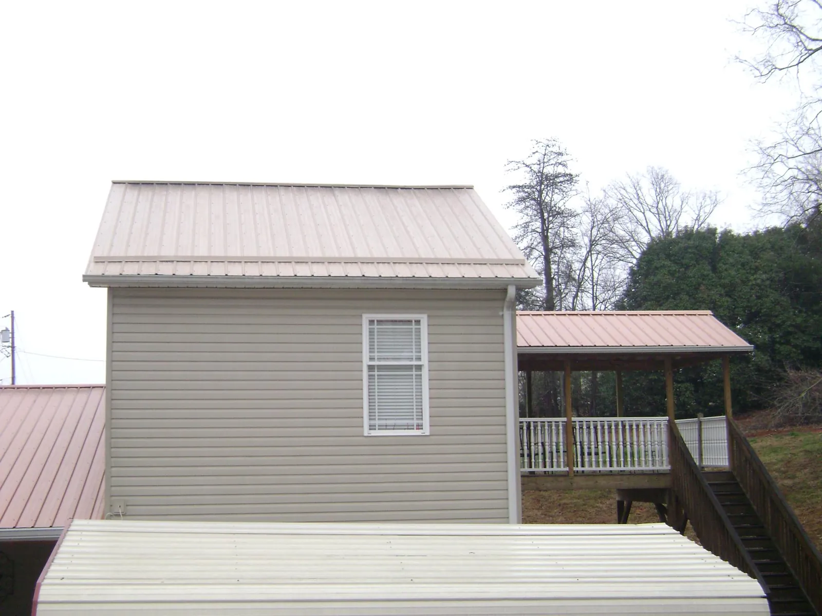 Tan metal roofs on a two story addition and attached porch, from a Roof Replacement job in Clarendon
